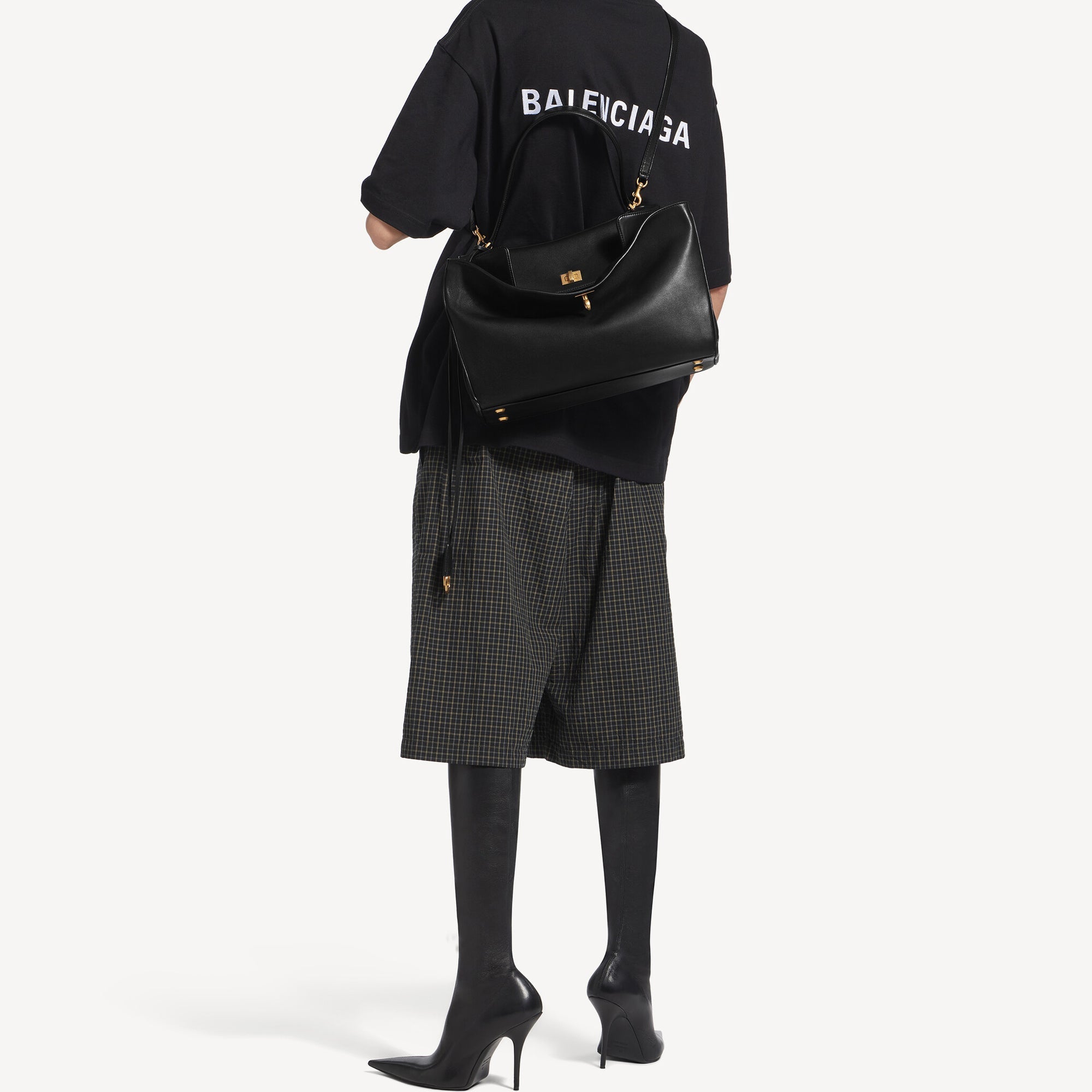 A model wearing a Rodeo style slouchy medium tote bag in black with brassy gold hardware