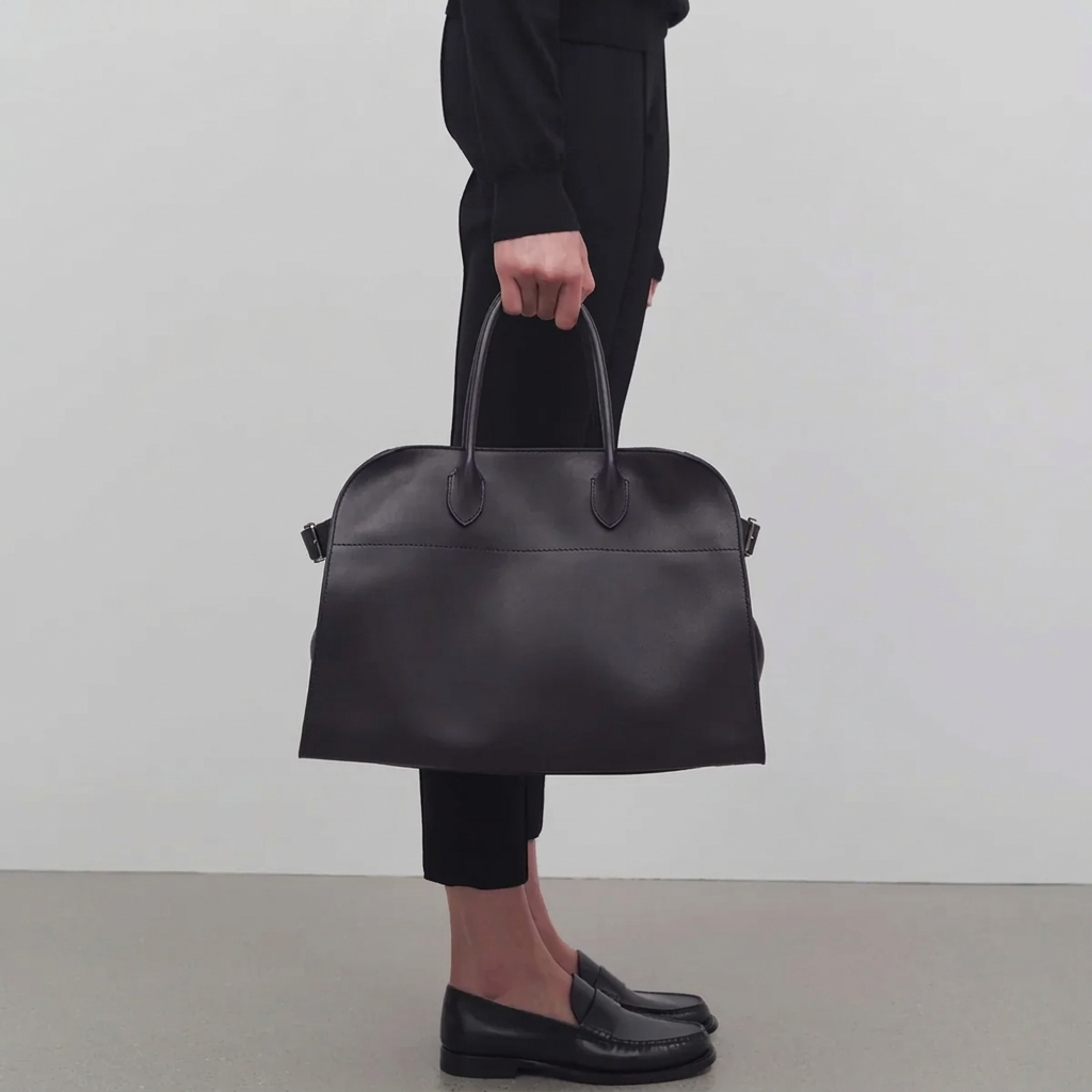 Model holding black leather large tote bag with toggle closure and side tabs, silver hardware